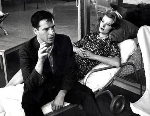 Black-and-white photograph of a seated man gesturing beside a reclining woman.